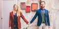 couple in vintage-looking clothing standing in front of a wall with red framed pictures